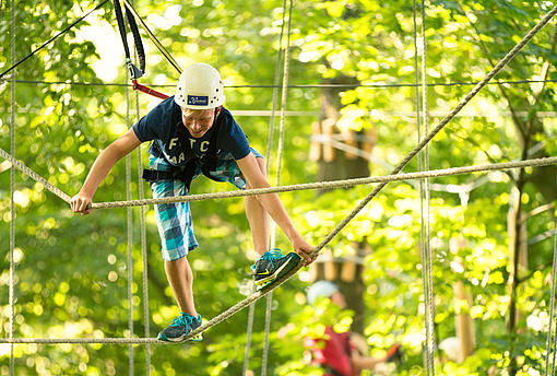 Junge im Kletterpark balanciert auf einem Seil