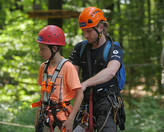 Mitarbeiter kontrolliert den Klettergurt eines jungen Teilnehmers